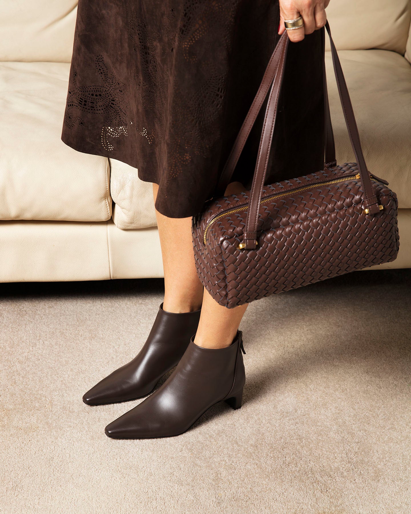 Person wearing dark brown ankle boots and holding a matching handbag indoors.