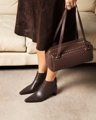 Person wearing dark brown ankle boots and holding a matching handbag indoors.